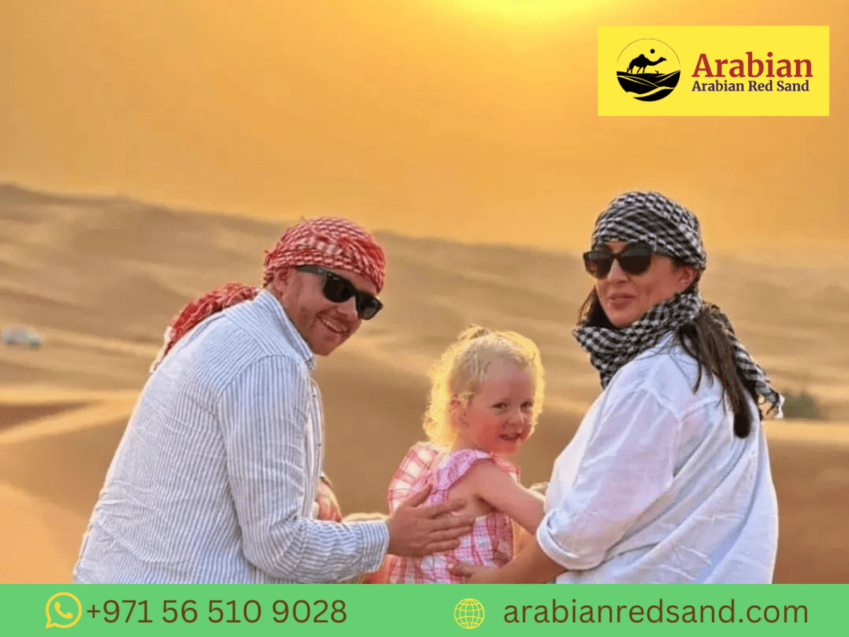 A group of 3–4 friends laughing on red dunes, wearing casual desert attire, quad bikes in background, clear desert sky with evening glow.